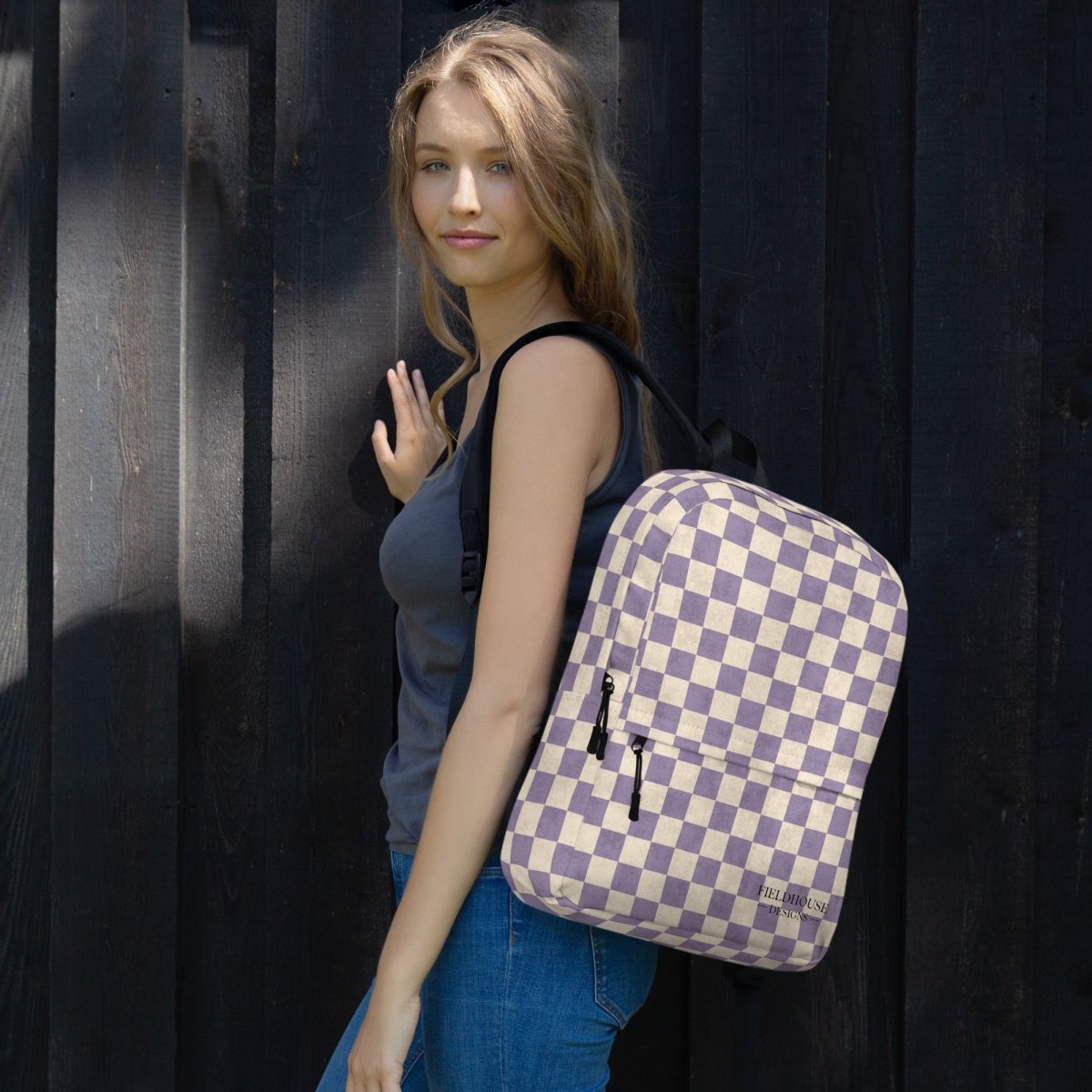Woman with a checkered backpack standing against a dark wall