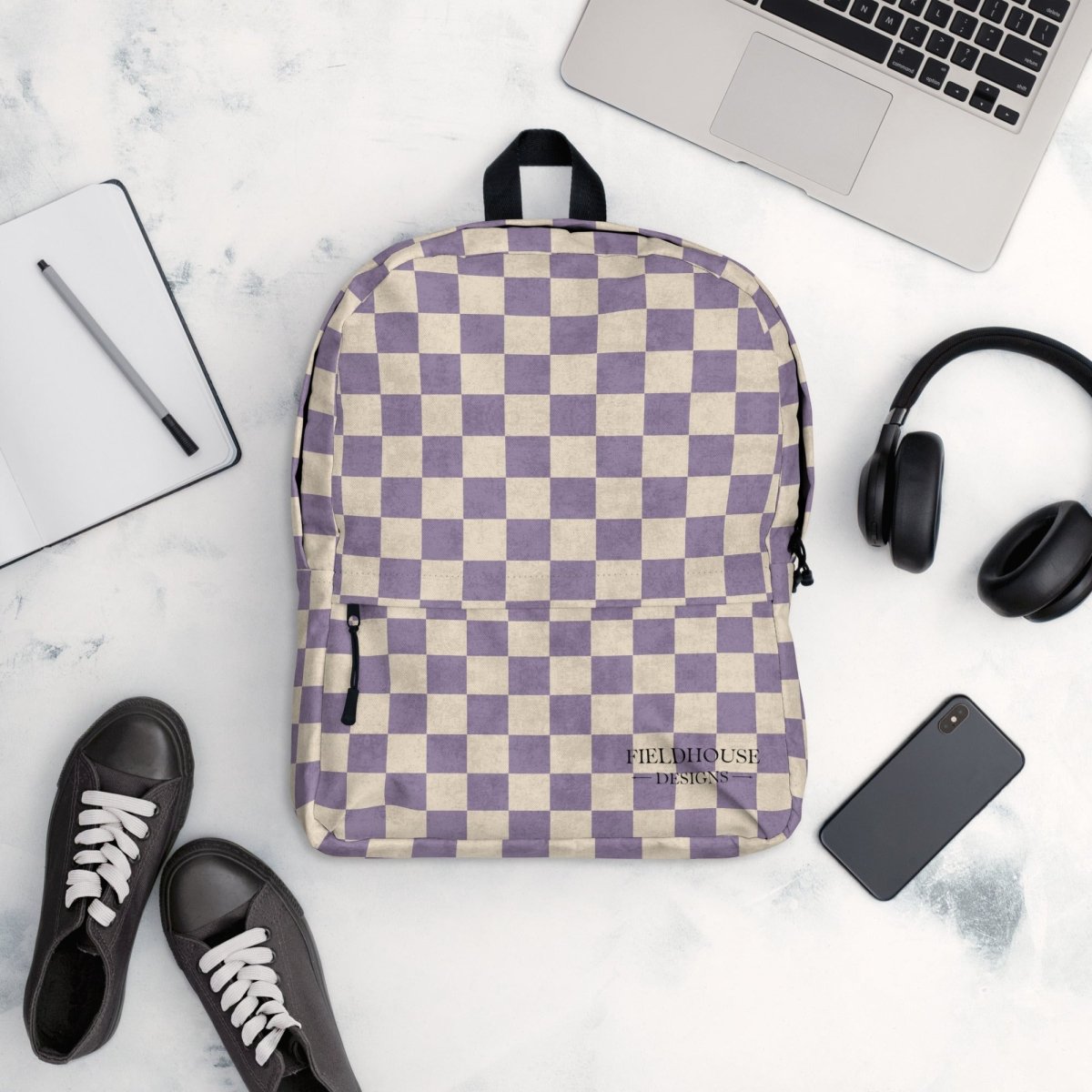 Checkered backpack on a marble surface with a laptop, headphones, and shoes.