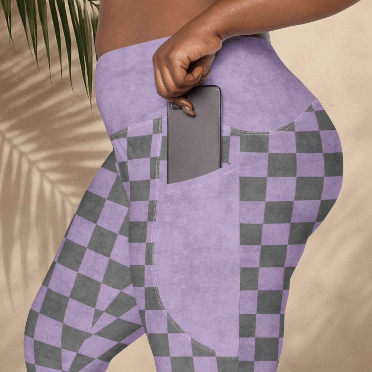 Person wearing purple and gray checkered leggings with a pocket holding a phone, against a beige background.