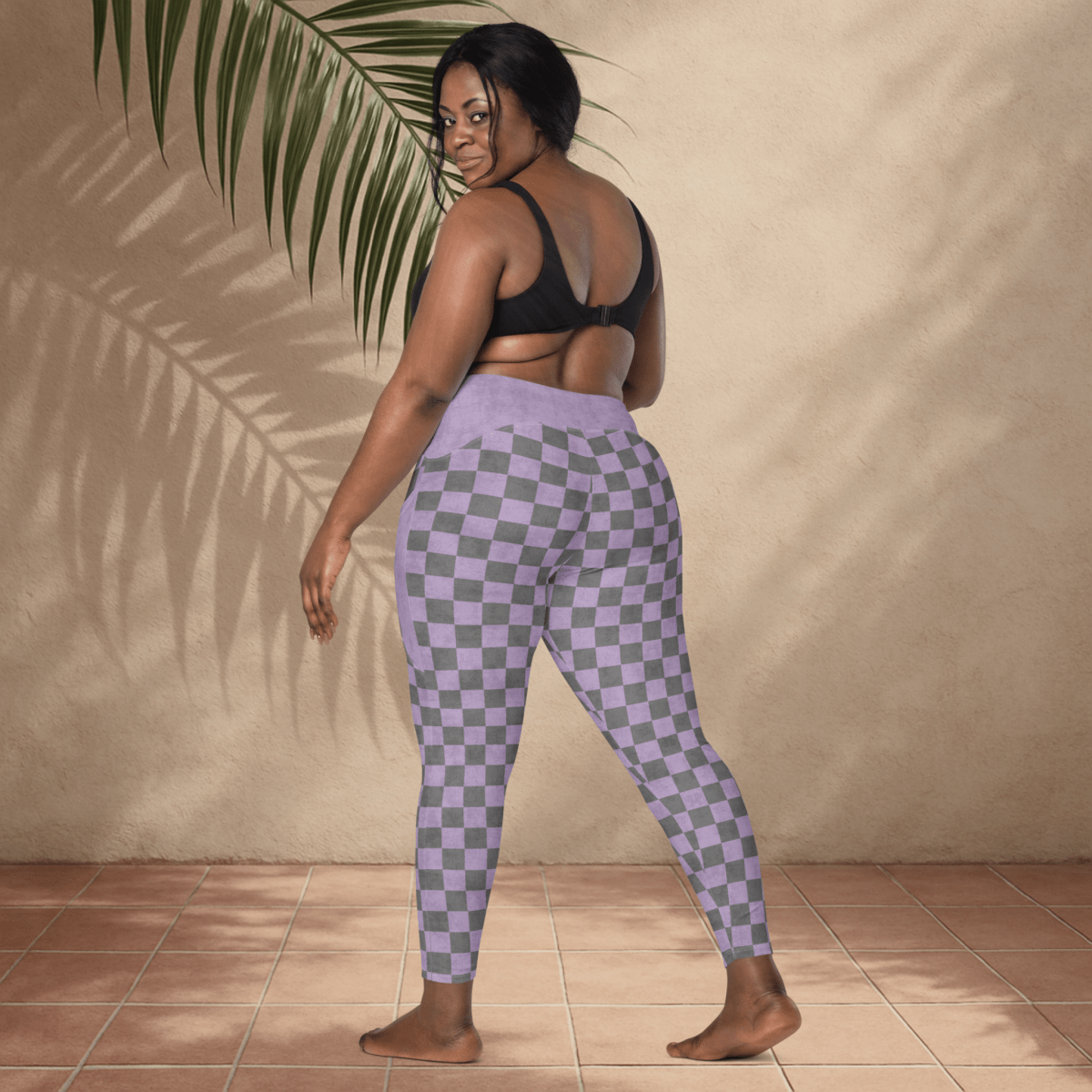 Woman wearing checkered leggings and a black sports bra against a beige wall.