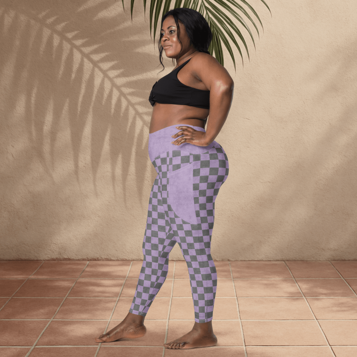 Woman wearing a black sports bra and purple checkered leggings standing against a beige wall.