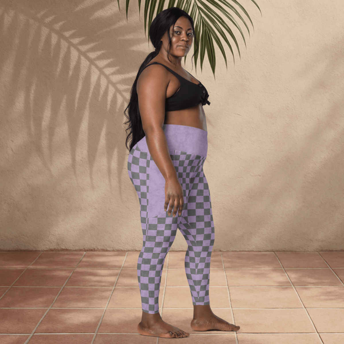 Woman wearing checkered leggings standing against a beige wall with a plant.