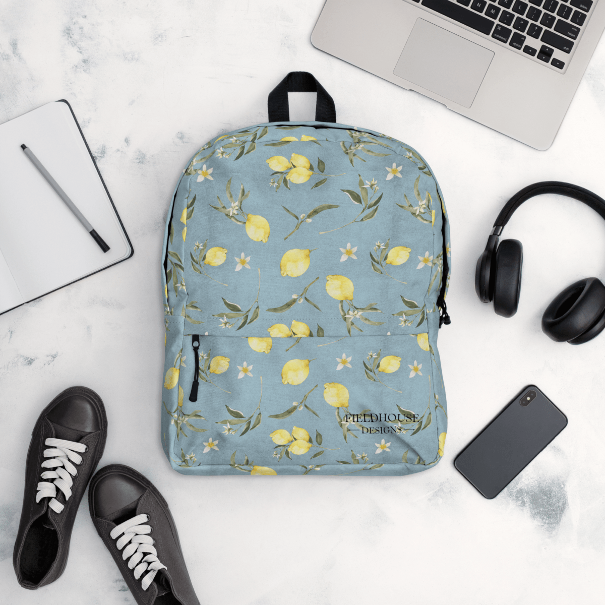 Blue floral backpack with lemons on a white surface with a laptop, headphones, and shoes.