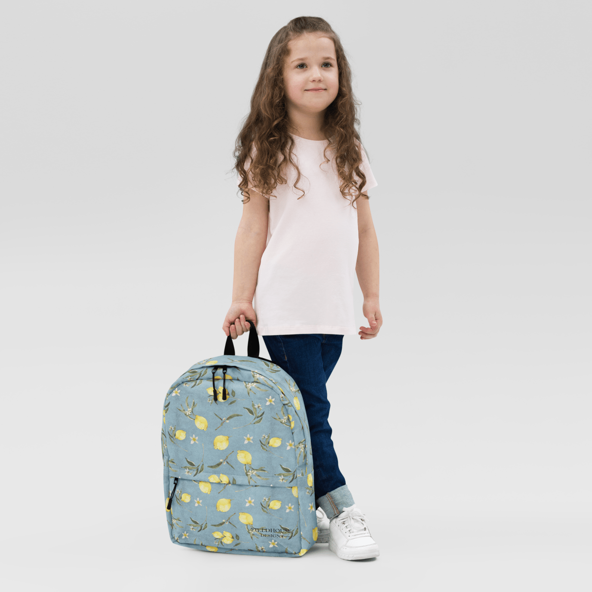 Young girl holding a blue backpack with yellow lemon pattern on a light gray background