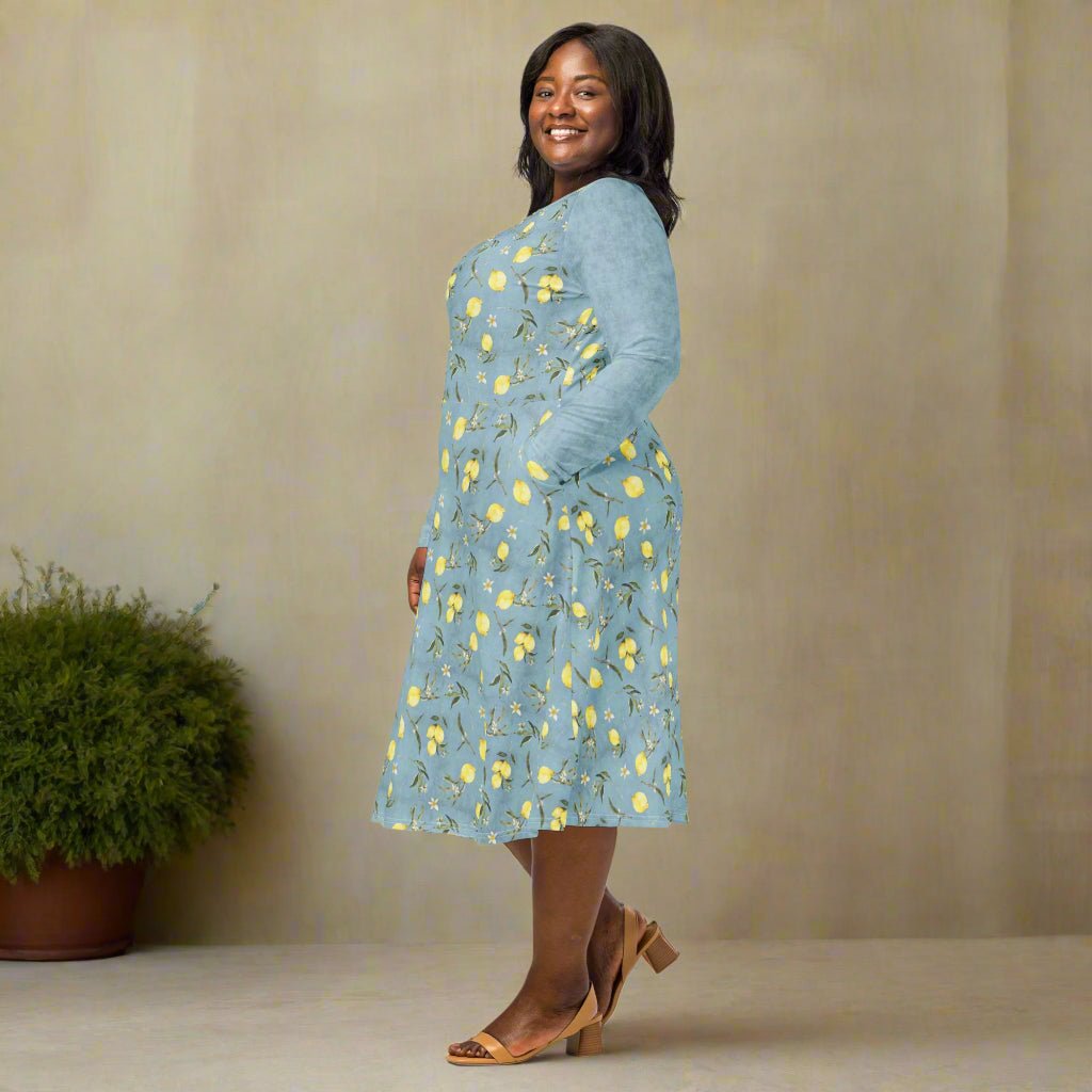 Woman wearing a blue floral dress standing against a beige wall with a plant in the background.