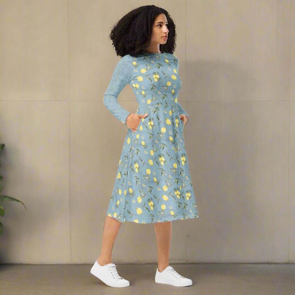 Woman wearing a blue dress with lemon floral pattern against a beige wall.
