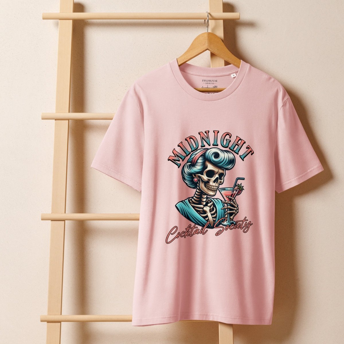 Pink t-shirt with skeleton graphic and text on a wooden hanger against a beige background