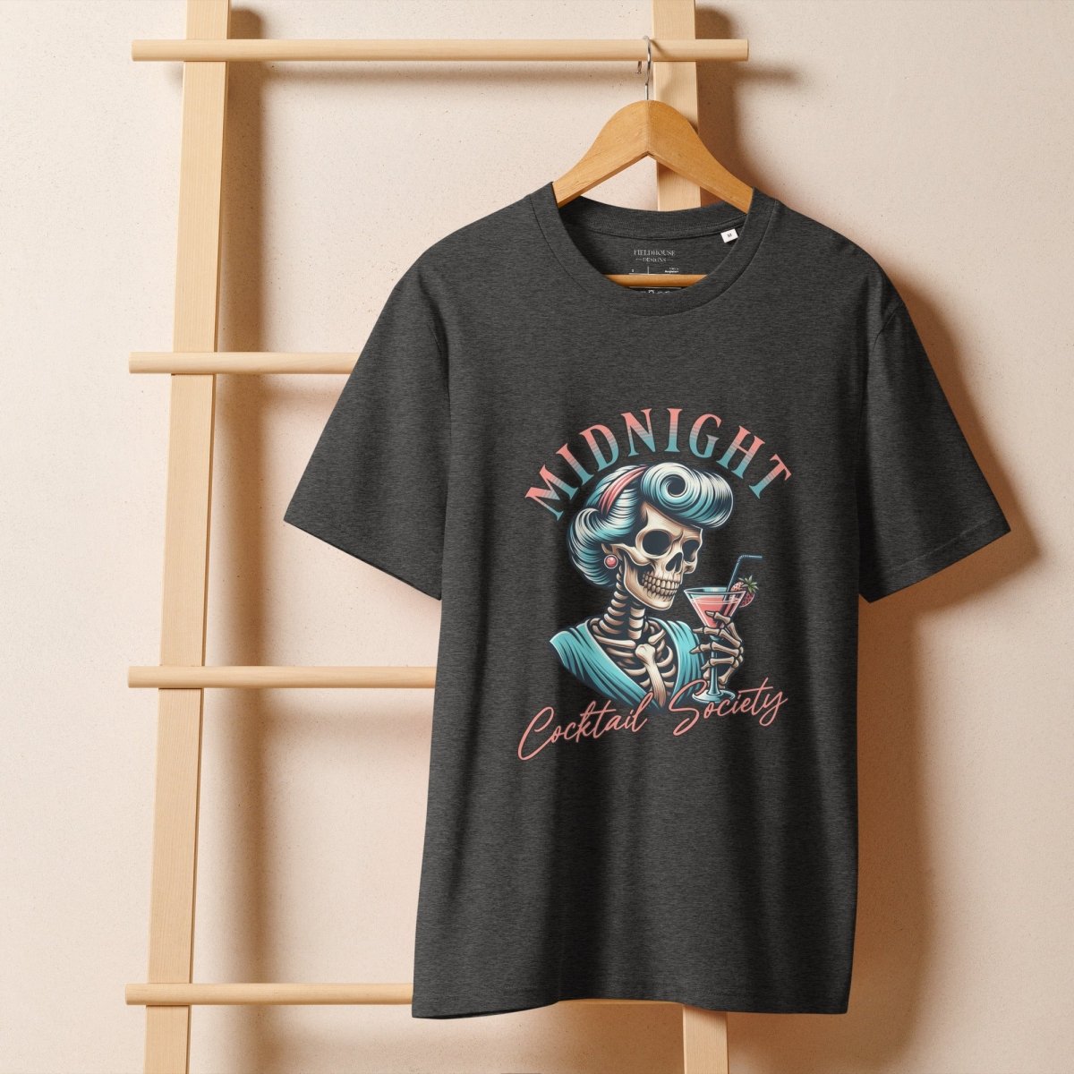 Black t-shirt with skeleton design and 'Midnight Cocktail Society' text on a wooden hanger against a beige background.