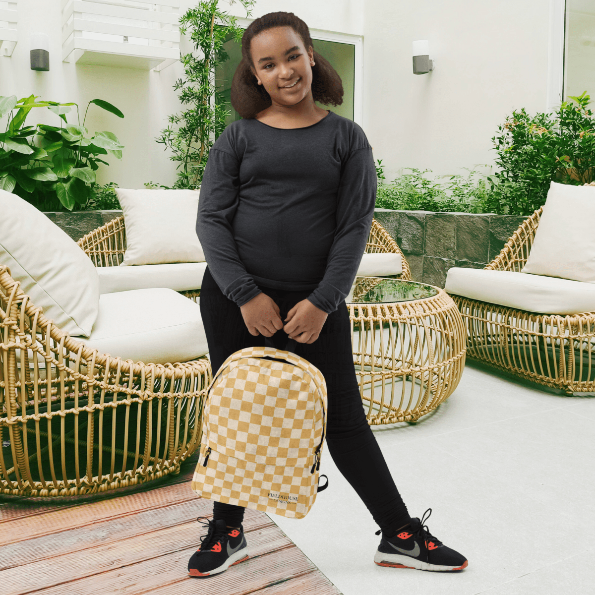 Person holding a checkered backpack in an outdoor setting with wicker furniture and plants.