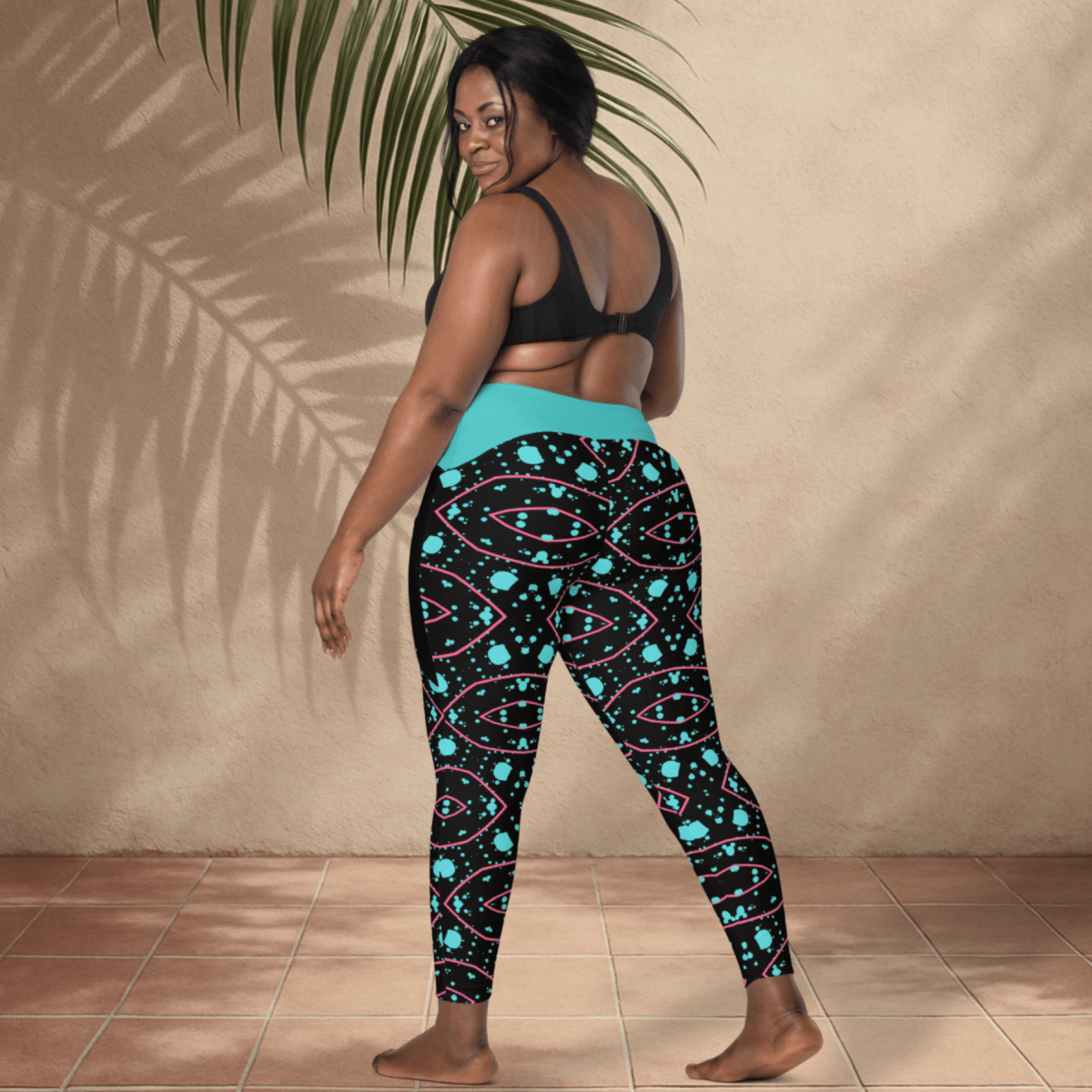 Woman wearing black patterned leggings with a blue top, standing against a beige wall.