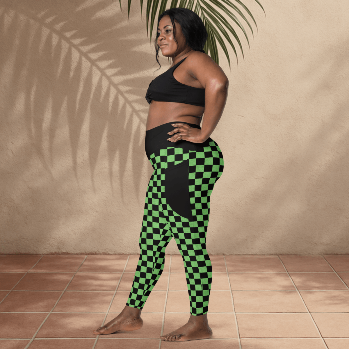 Woman wearing a black sports bra and green checkered leggings standing against a beige wall.