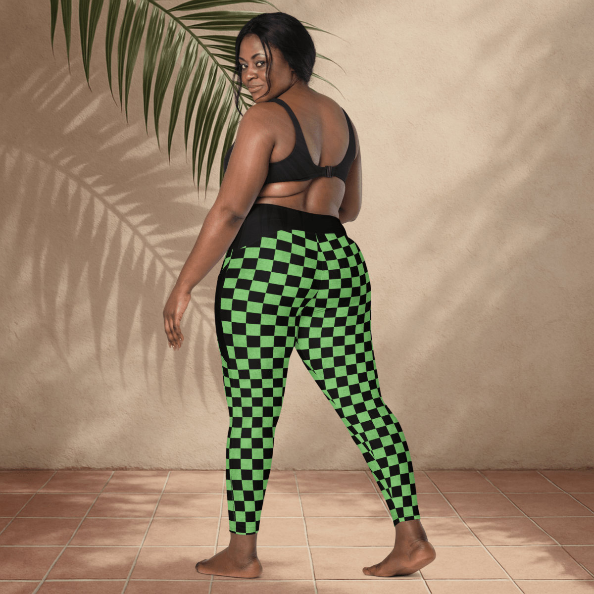 Woman wearing green and black checkered pants standing against a beige wall.