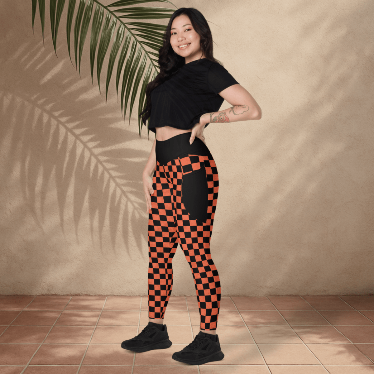 Woman wearing black and orange checkered leggings with a black top against a beige wall.