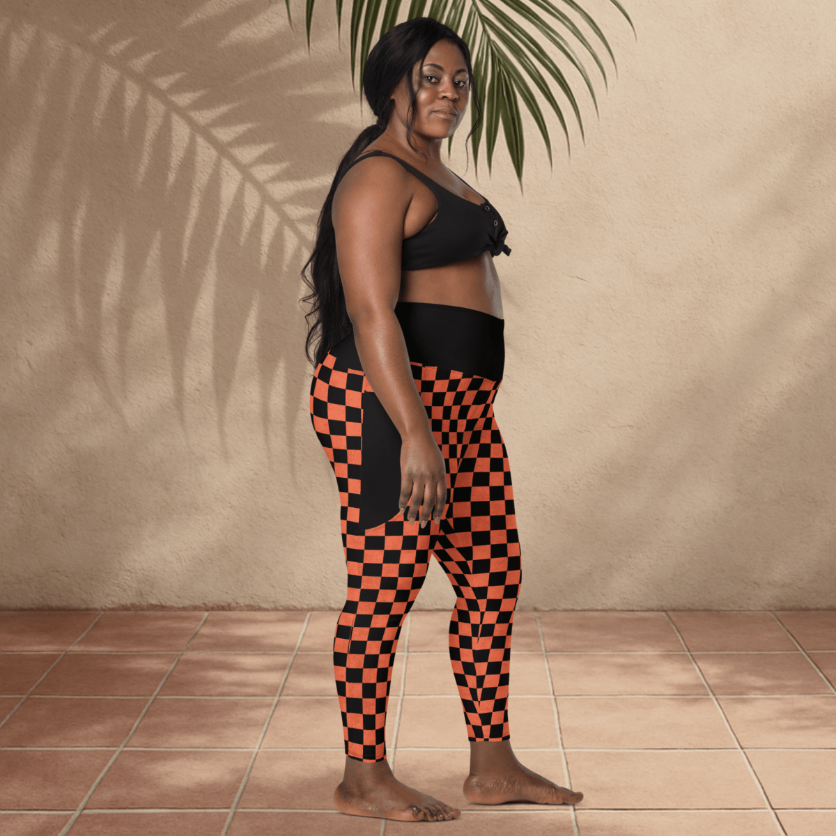 Woman wearing black and orange checkered leggings against a beige wall.