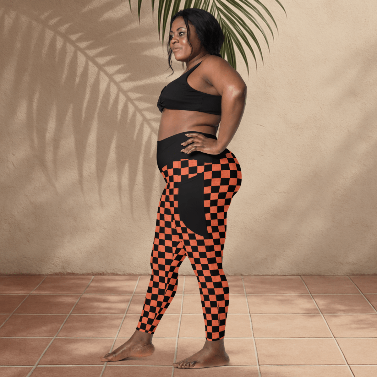 Woman wearing black and orange checkered leggings and black sports bra against a beige wall.
