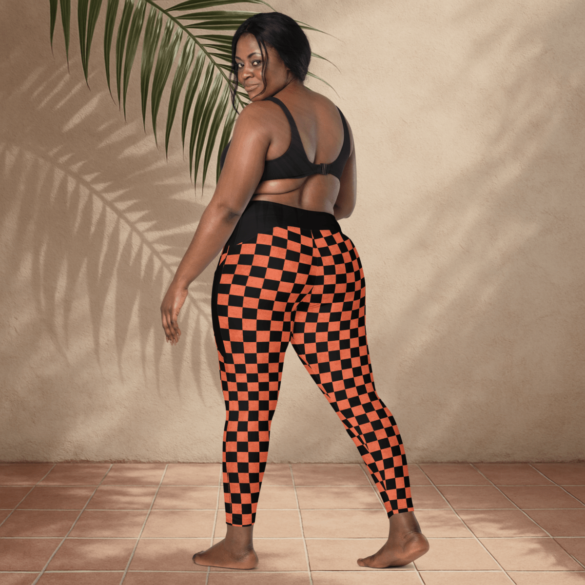 Person wearing black and orange checkered leggings against a beige wall.