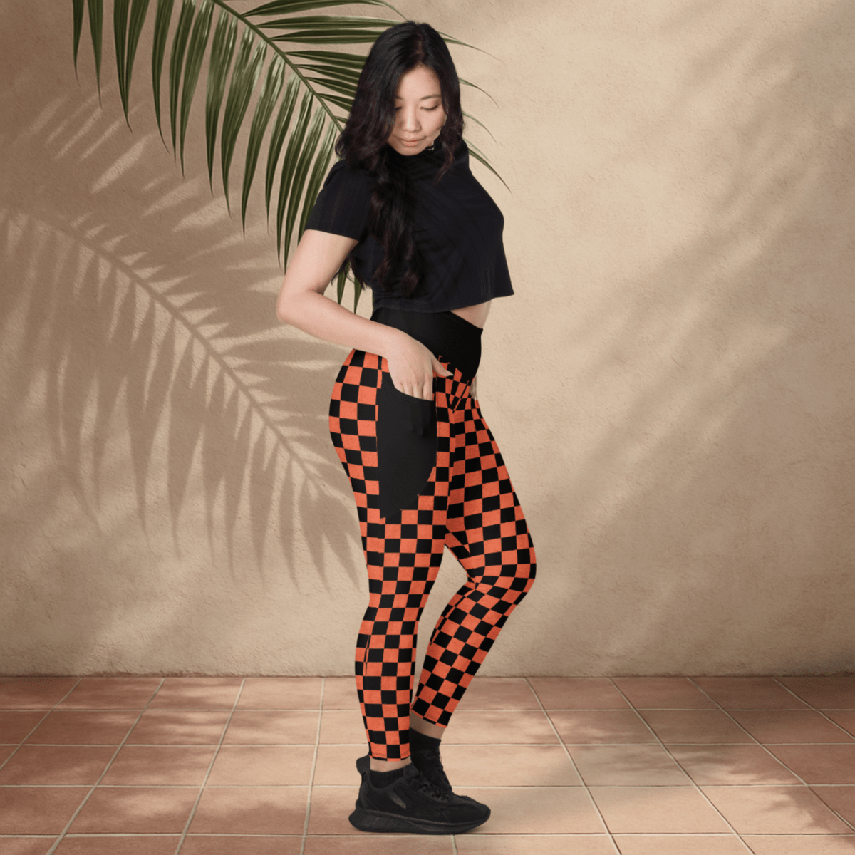 Woman wearing black and orange checkered pants against a beige wall.