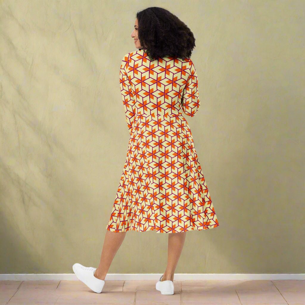 Woman wearing a patterned dress standing against a plain wall.
