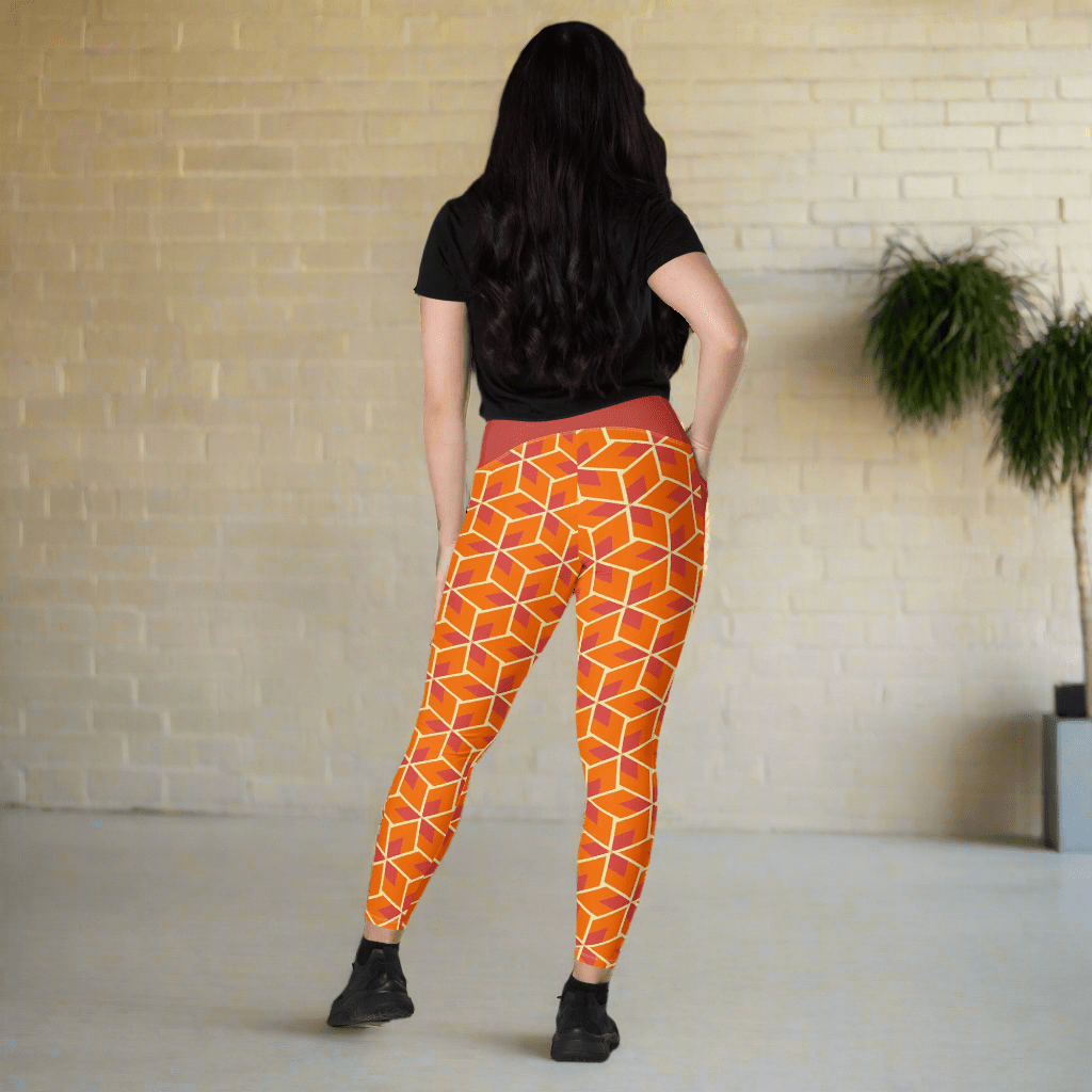 Person wearing orange geometric leggings standing in a room with a brick wall and plants.