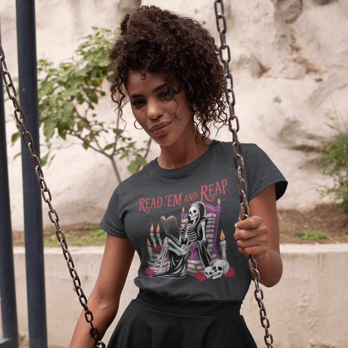 Woman swinging on a swing set wearing a graphic t-shirt and black skirt.