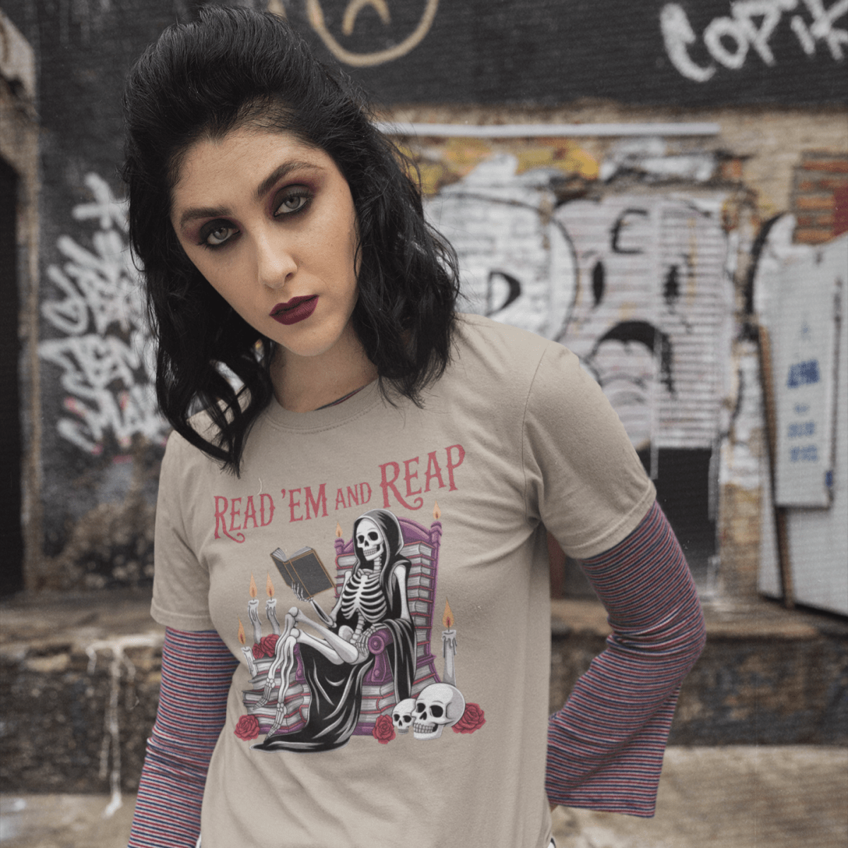 Woman wearing a graphic t-shirt with a skeleton and text design, standing in an urban setting with graffiti.