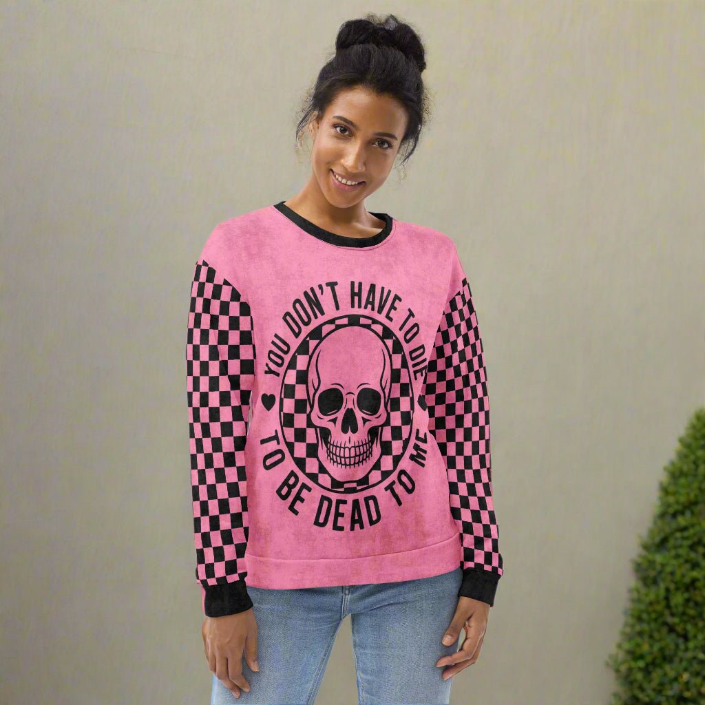 Person wearing a pink sweatshirt with a skull design and text on a neutral background