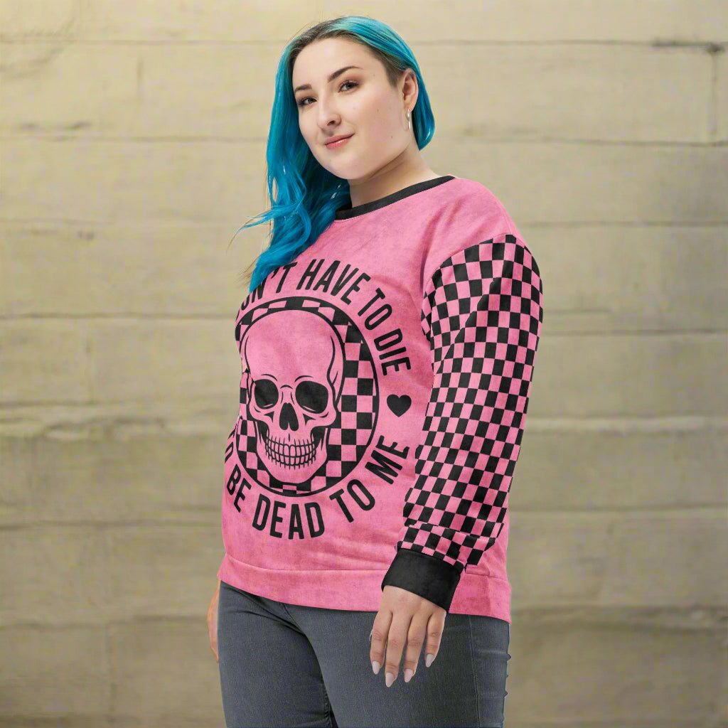 Person wearing a pink sweatshirt with a skull design and text against a beige brick wall.
