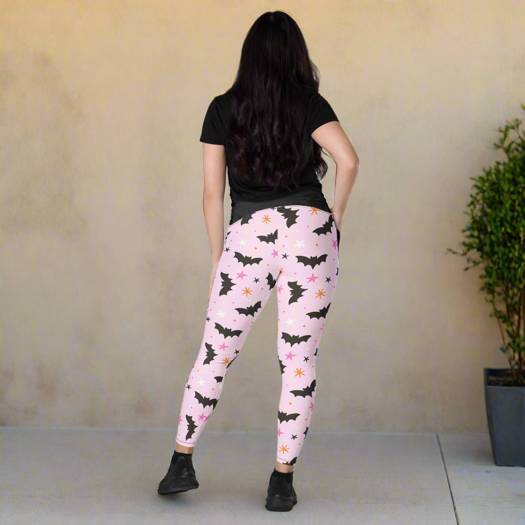 Person wearing pink leggings with black bat pattern against a beige wall.
