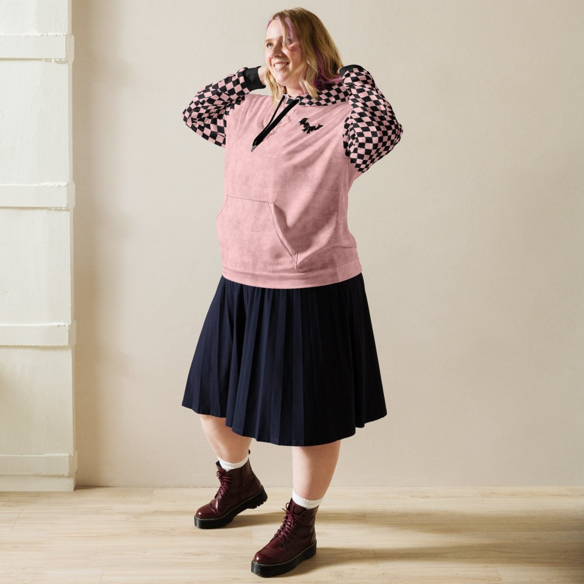 Person wearing a pink hoodie, black skirt, and maroon boots indoors.