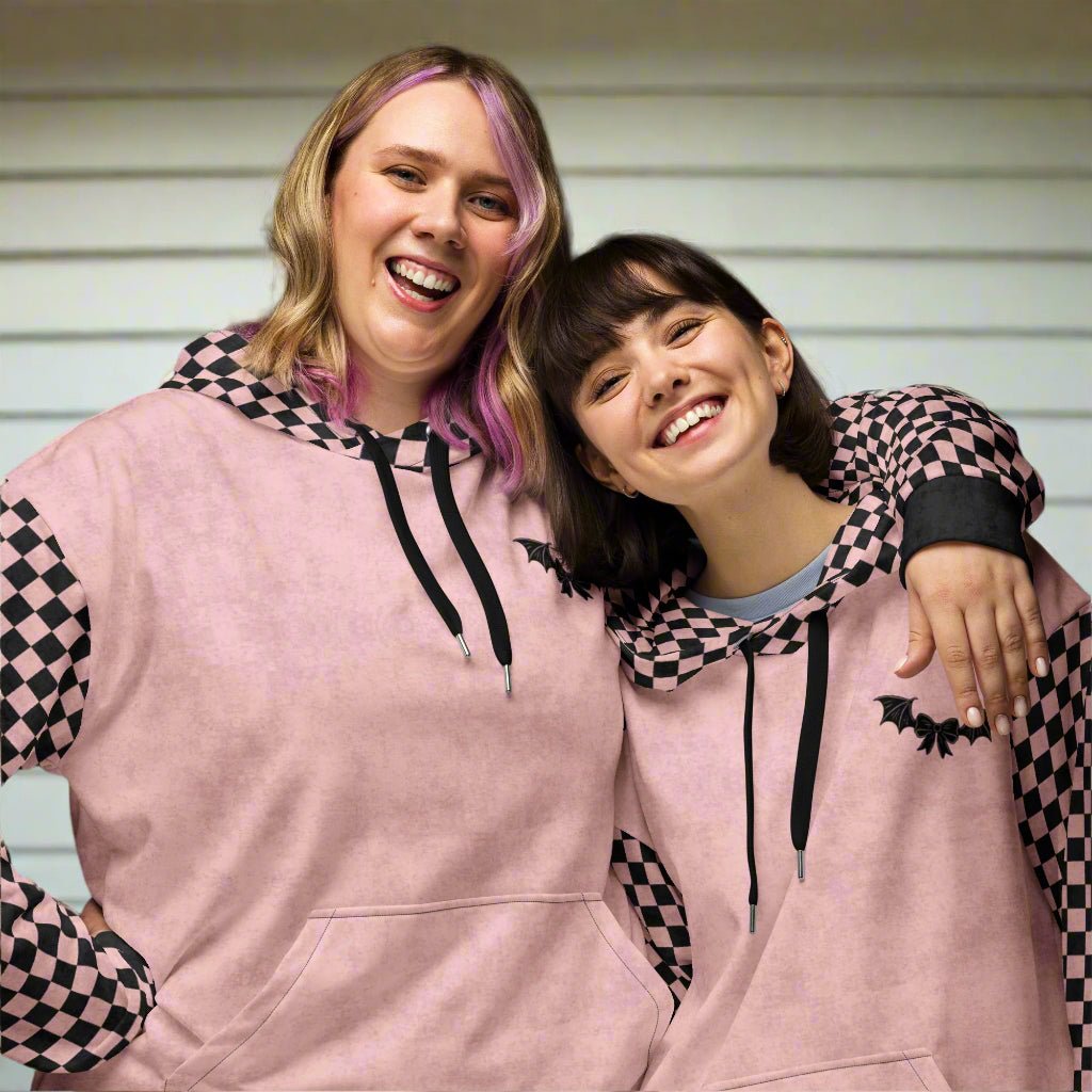 Two people wearing matching pink hoodies with black checkered sleeves and bat designs.