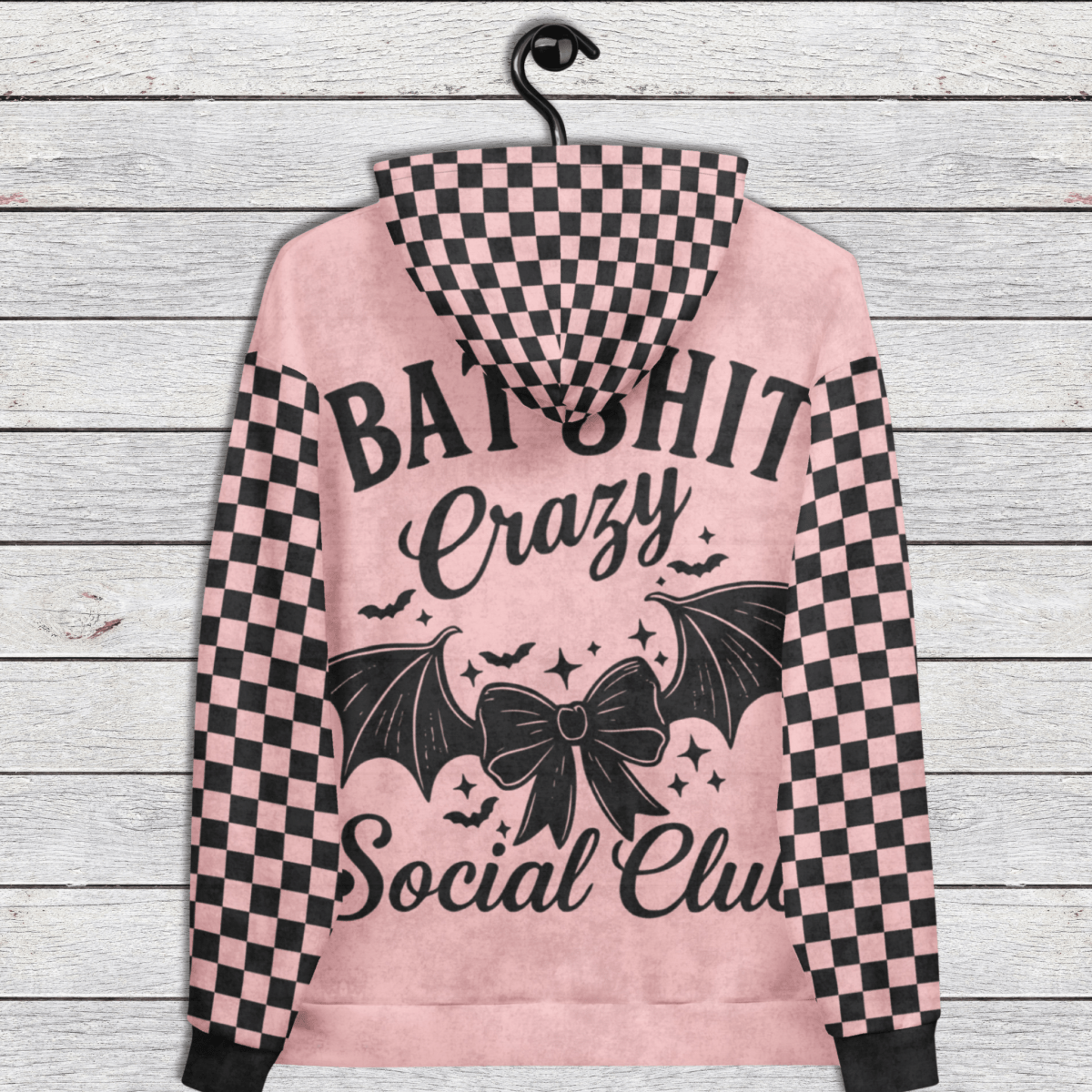 Pink hoodie with black checkered pattern and text on a wooden background