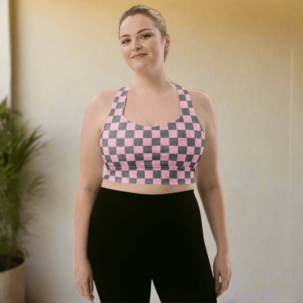 Woman wearing a pink and gray checkered sports bra and black leggings on a neutral background