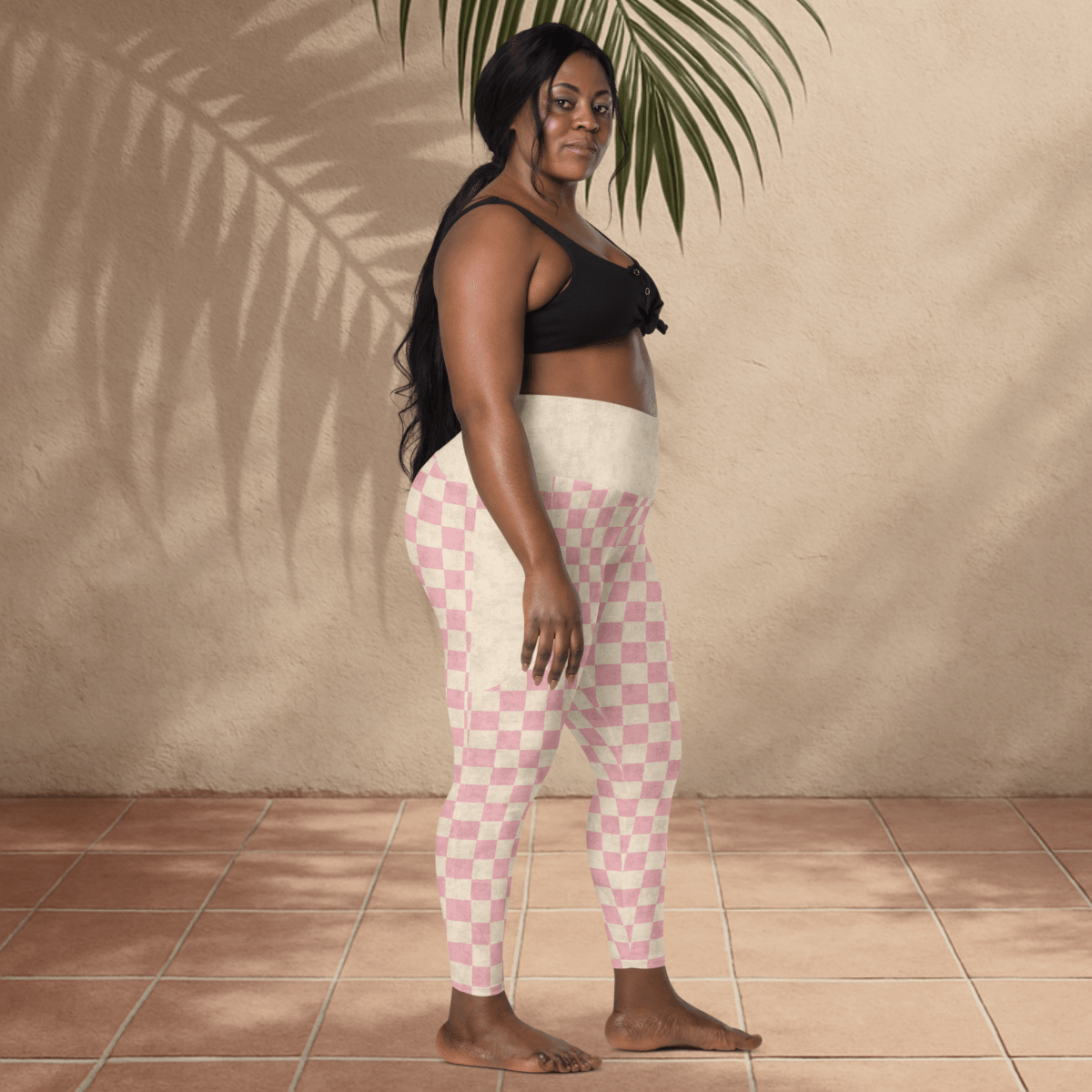 Woman wearing pink and white checkered pants against a beige wall.