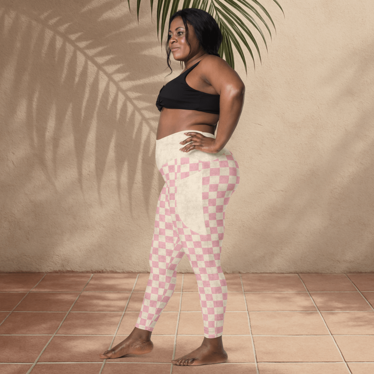 Woman wearing pink checkered leggings and black sports bra against a beige wall.