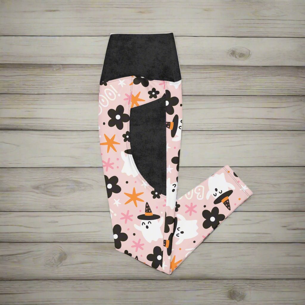 Leggings with Halloween-themed design featuring cats, pumpkins, and flowers on a pink background.