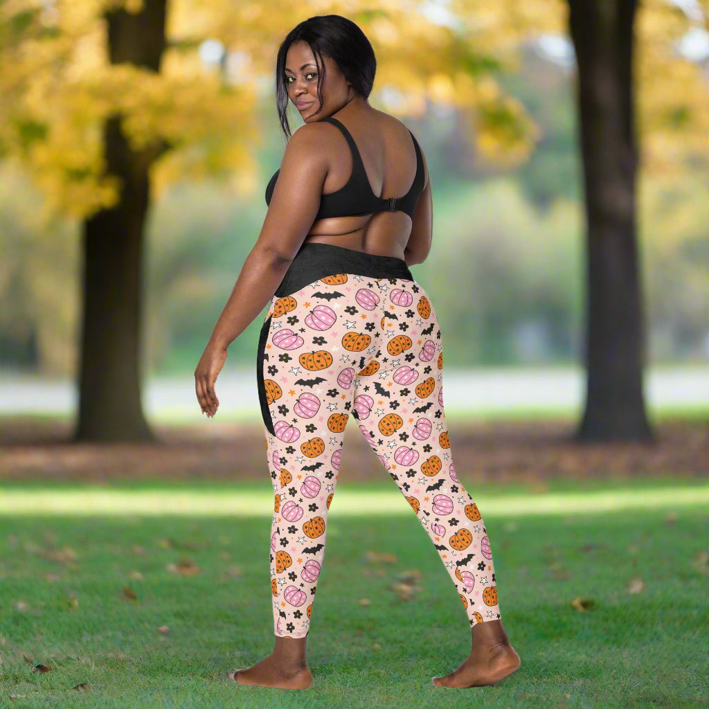 Woman wearing a black sports bra and Halloween leggings against a beige wall.