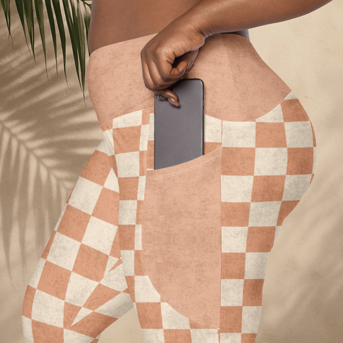 Person wearing checkered leggings with a phone in the pocket, against a neutral background.