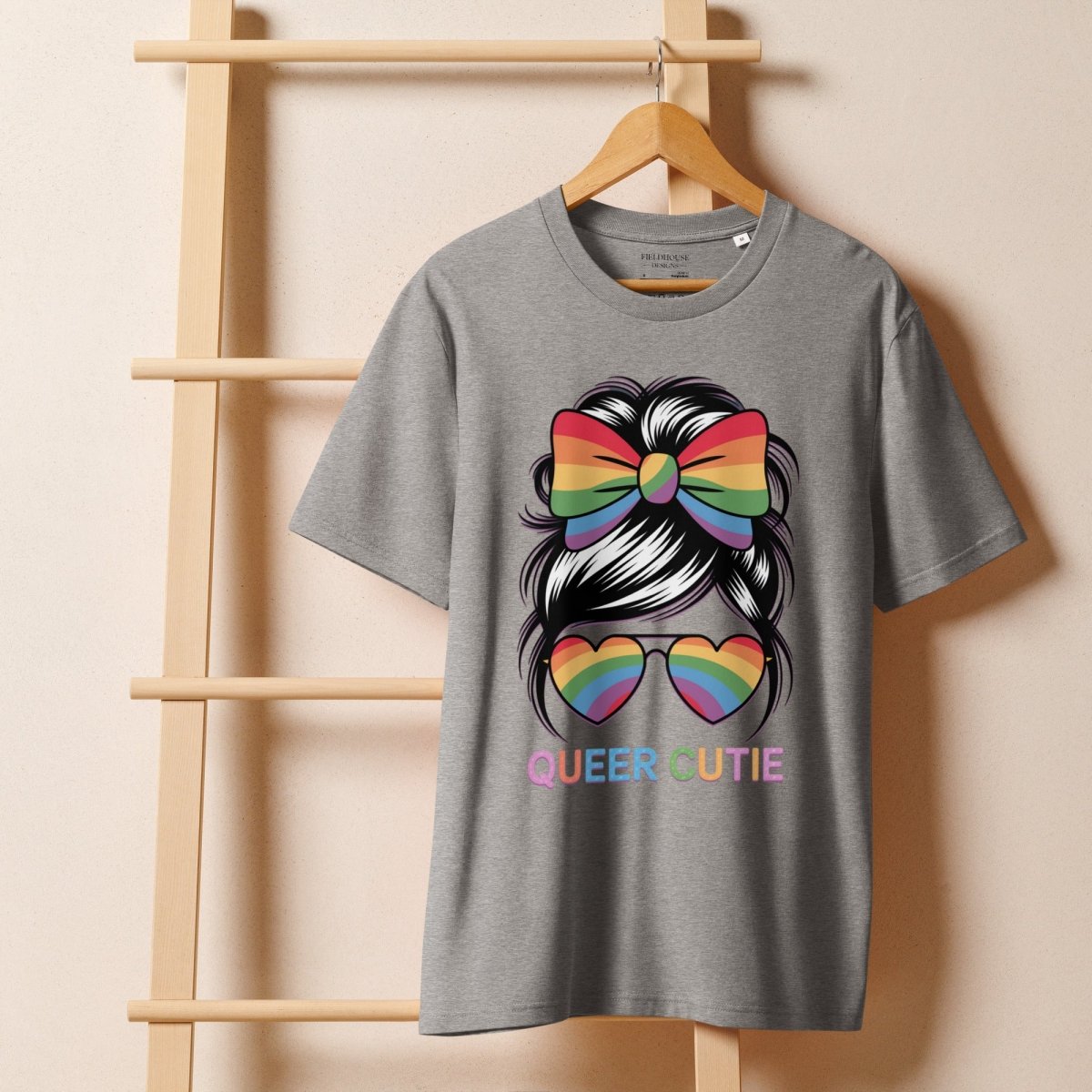 Gray t-shirt with rainbow bow and heart sunglasses design on a wooden hanger against a beige wall.