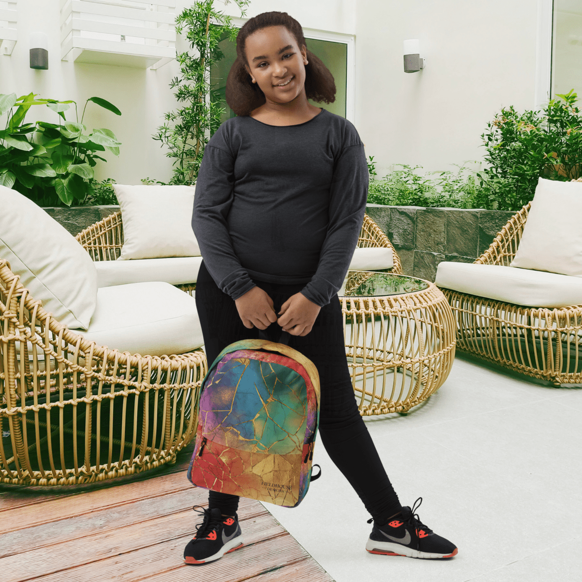 Person holding a colorful backpack in an outdoor setting with wicker furniture and plants.
