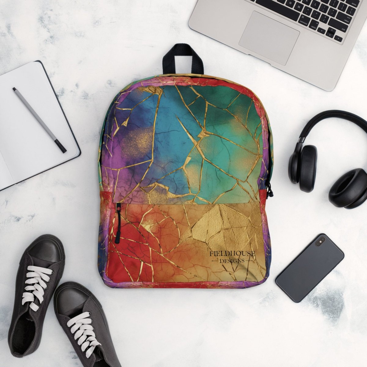 Colorful backpack with a marble pattern on a white surface with a laptop, phone, shoes, and headphones.