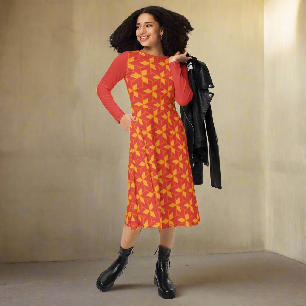 Woman wearing a red dress with yellow pattern, holding a black jacket against a beige wall.