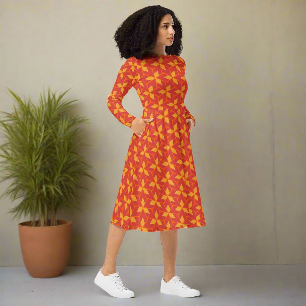Woman wearing a red and yellow patterned dress standing next to a potted plant against a beige wall.