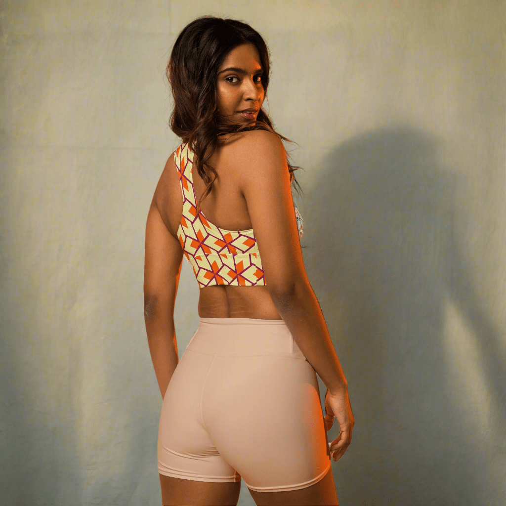 Woman wearing a patterned crop top and beige shorts against a warm gradient background