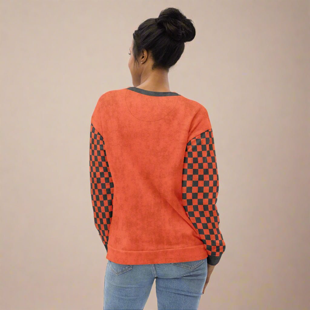 Person wearing an orange sweatshirt with checkered sleeves on a neutral background