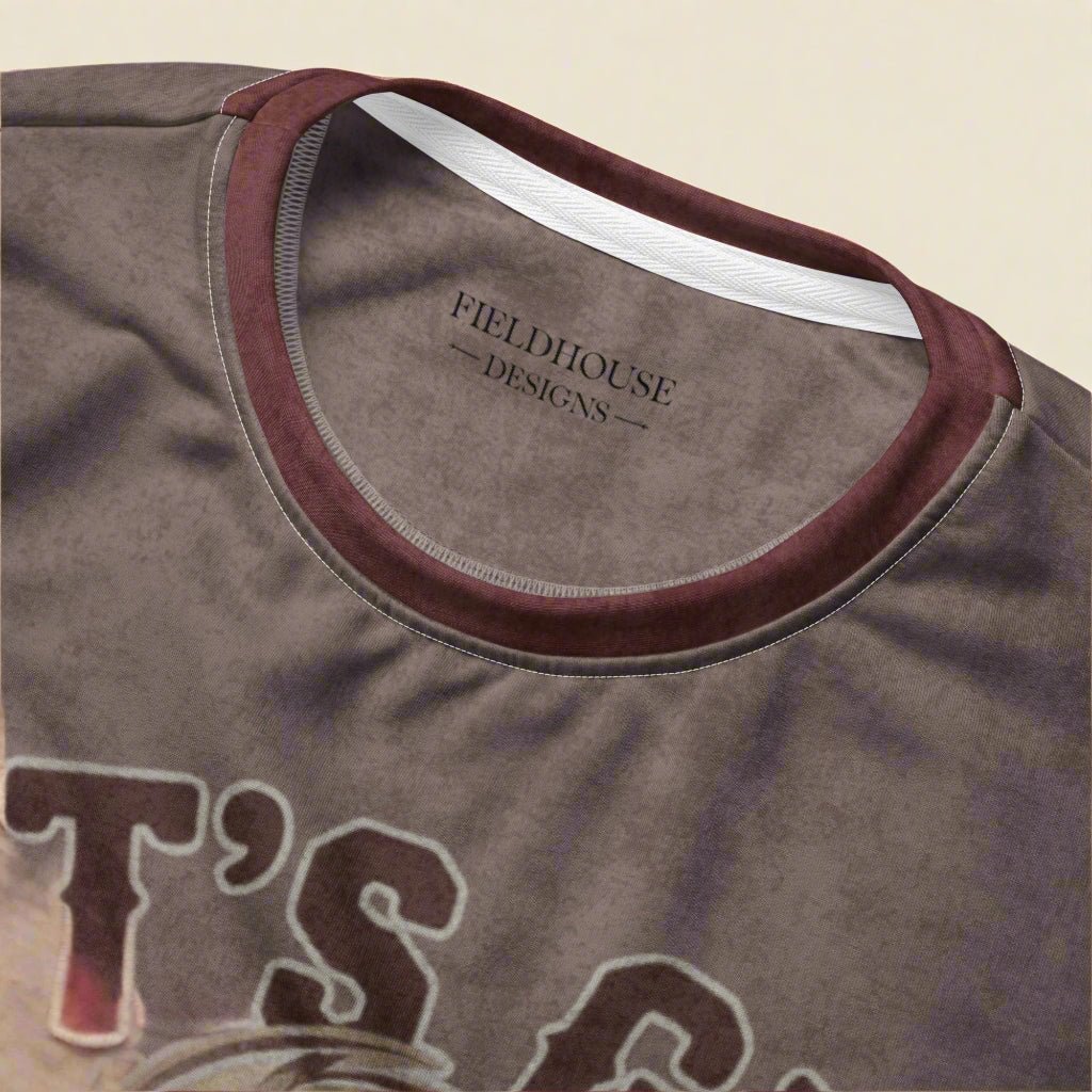 Close-up of a brown t-shirt with 'Fieldhouse Designs' logo on the collar.