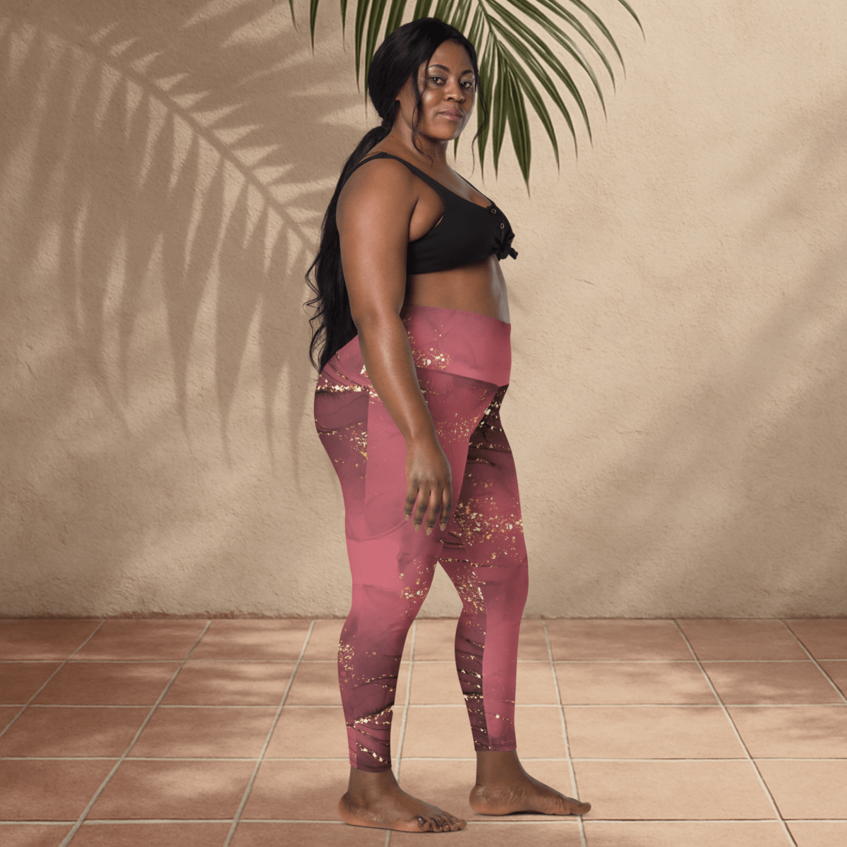 Woman wearing pink leggings with gold speckles against a beige wall.