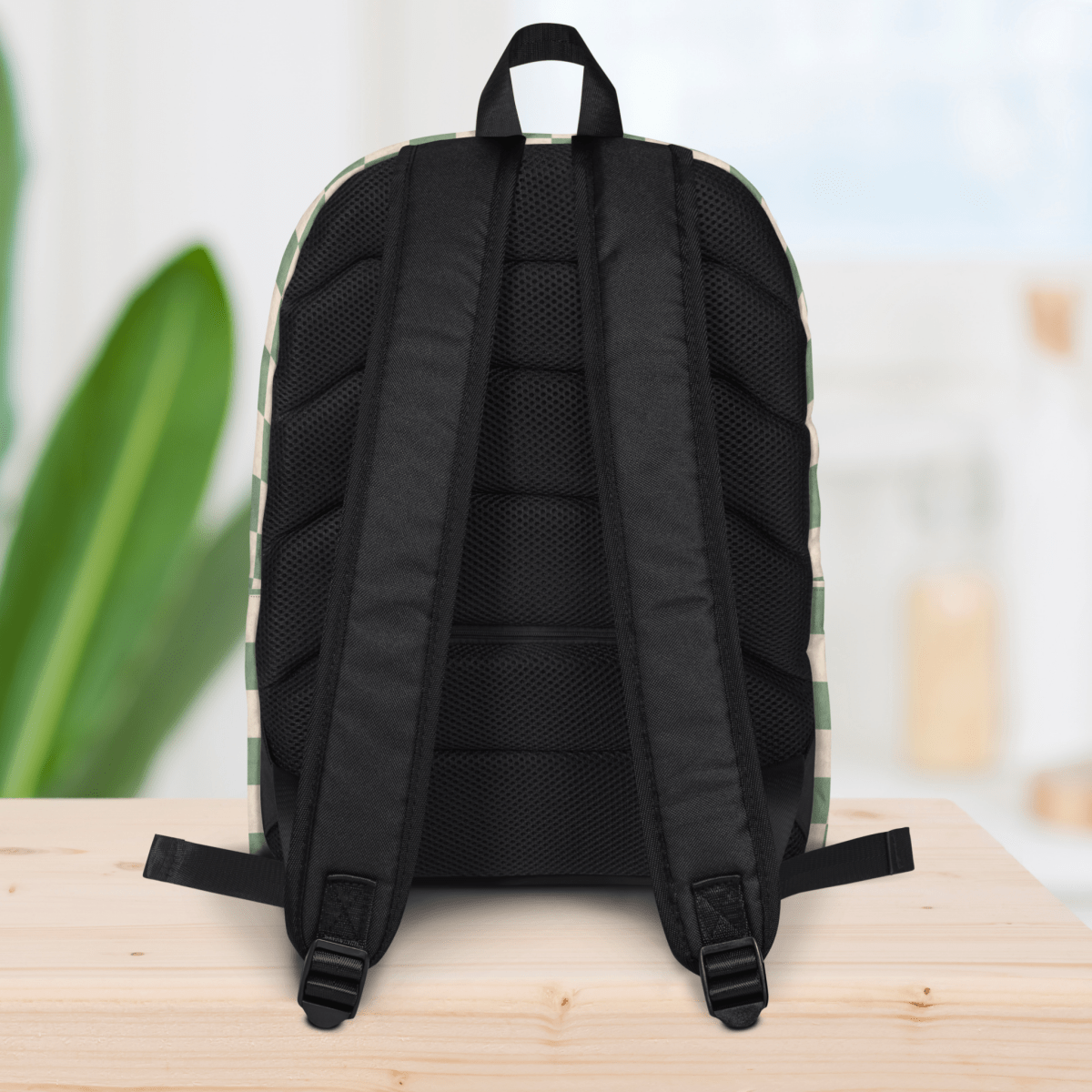 Backside of a backpack on a wooden surface with a blurred plant and light background