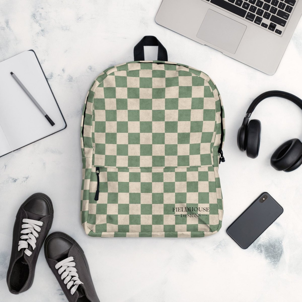 Checkered backpack on a marble surface with a laptop, headphones, and shoes.