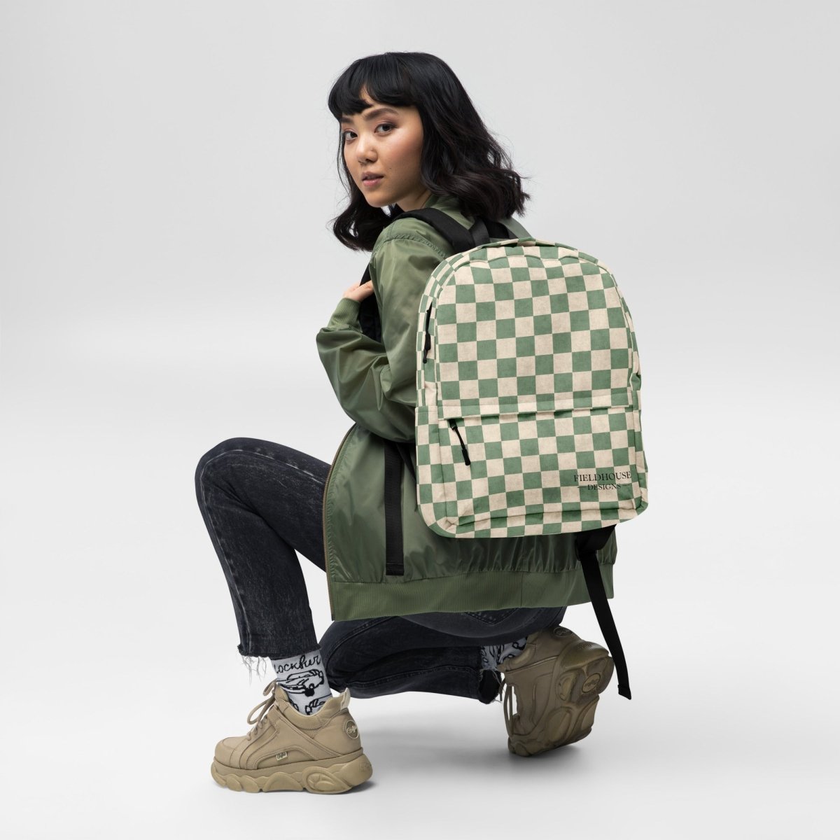 Person wearing a green and beige checkered backpack on a white background