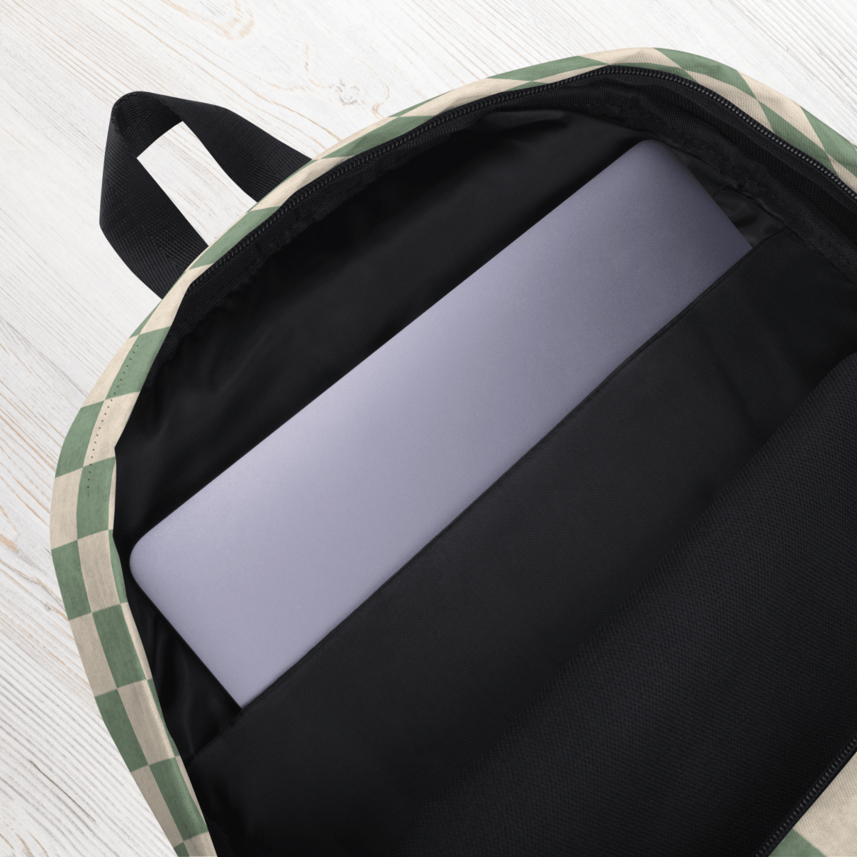 Sage green checkered backpack with a laptop inside on a light wooden surface
